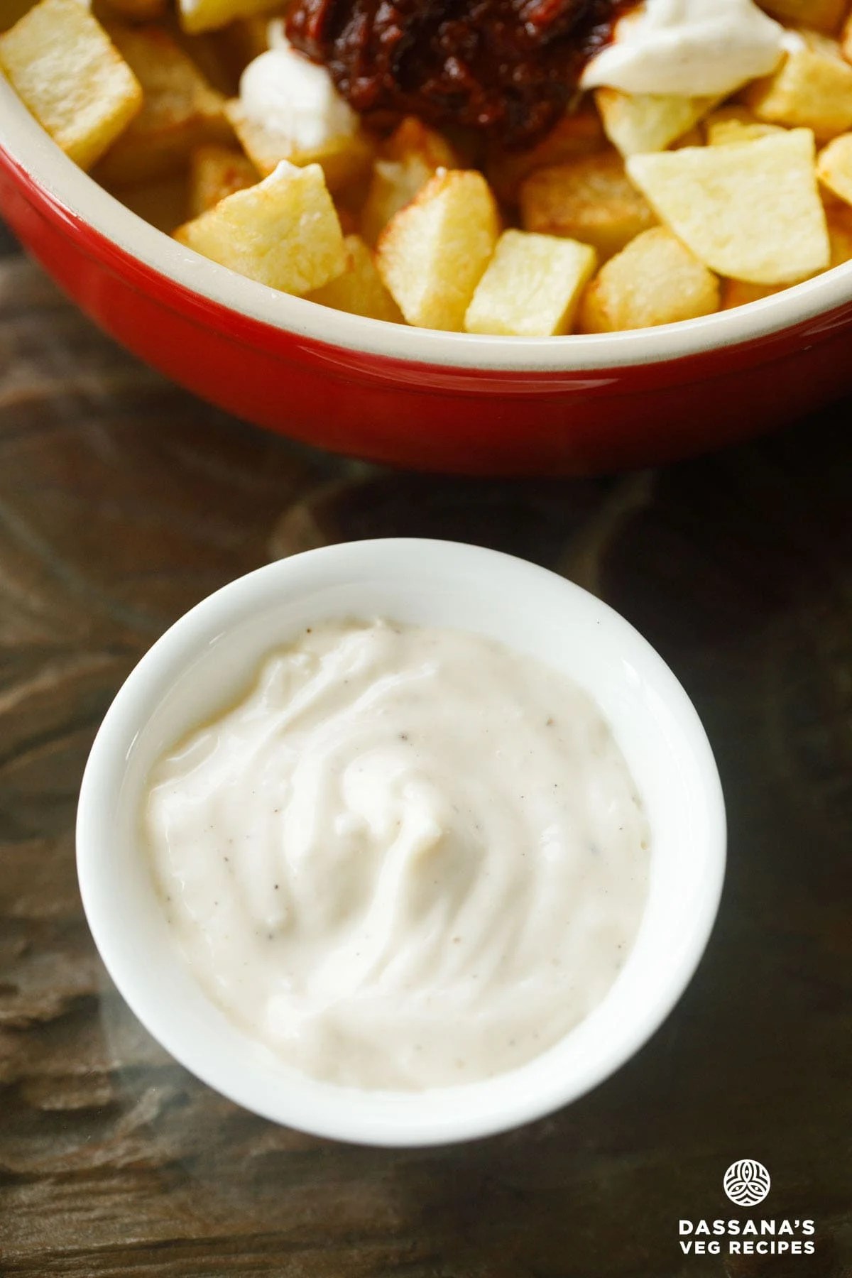 Aioli in a white bowl with fried potatoes in a red bowl placed on top.