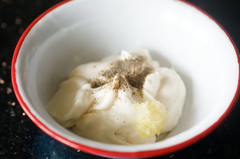 Garlic, seasonings with mayo in bowl to make aioli recipe.