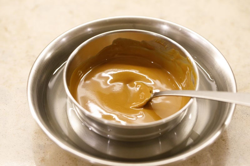 Melted biscoff spread in the bowl placed on a plate filled with water.