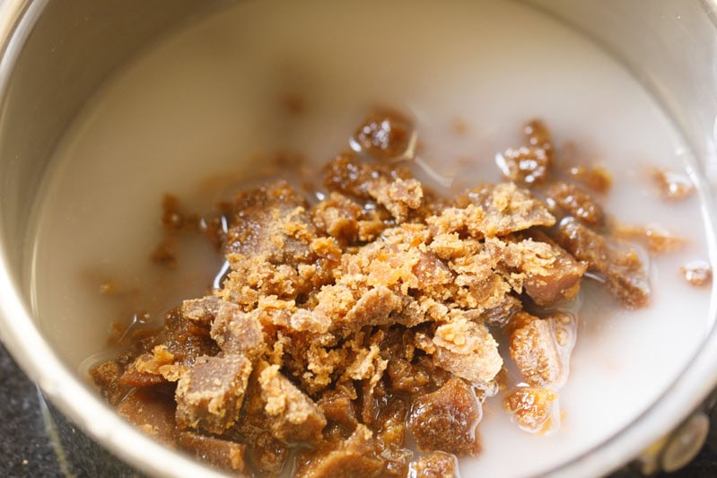 Mound of chopped jaggery on thin coconut milk in pan.