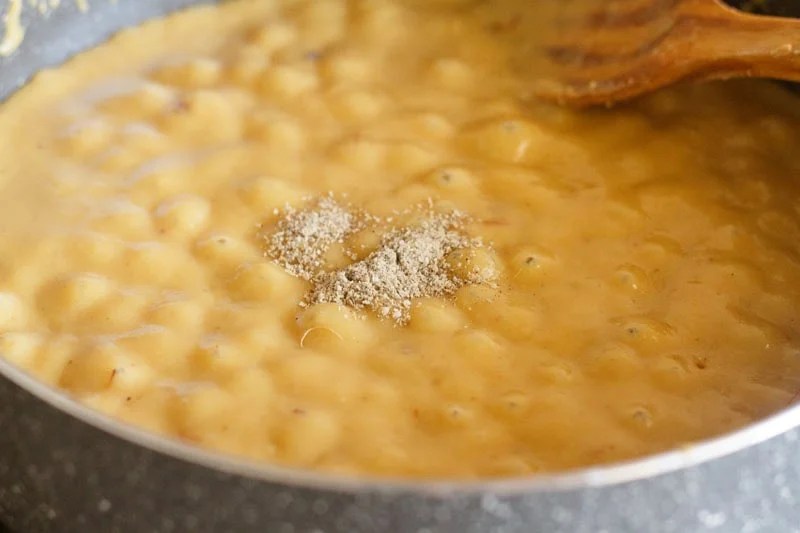 Cardamom powder on the bubbling mawa mixture in pan.