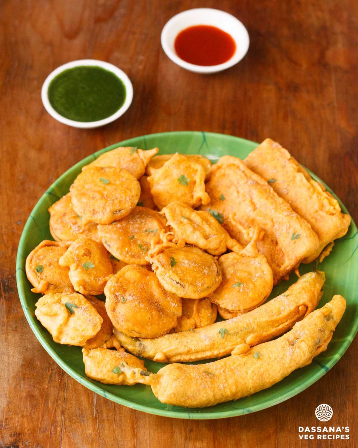 Assorted bhajia on a plate with chutneys in separate bowls.