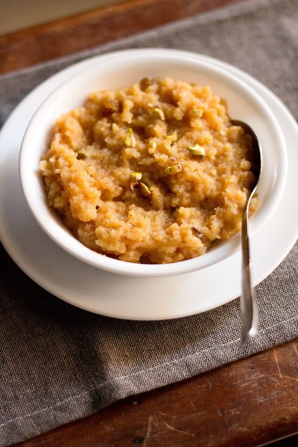 moong dal halwa served in a white bowl kept on a white plate with a spoon inside the bowl.