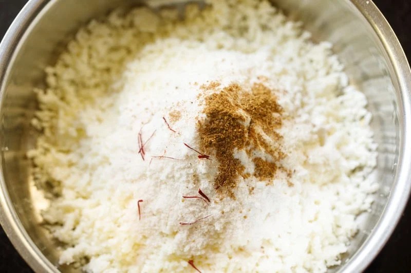 Grated paneer in bowl with saffron strands and spices.