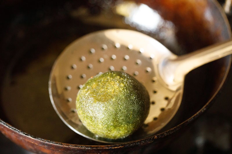 Fried palak kofta on a slotted metal spoon