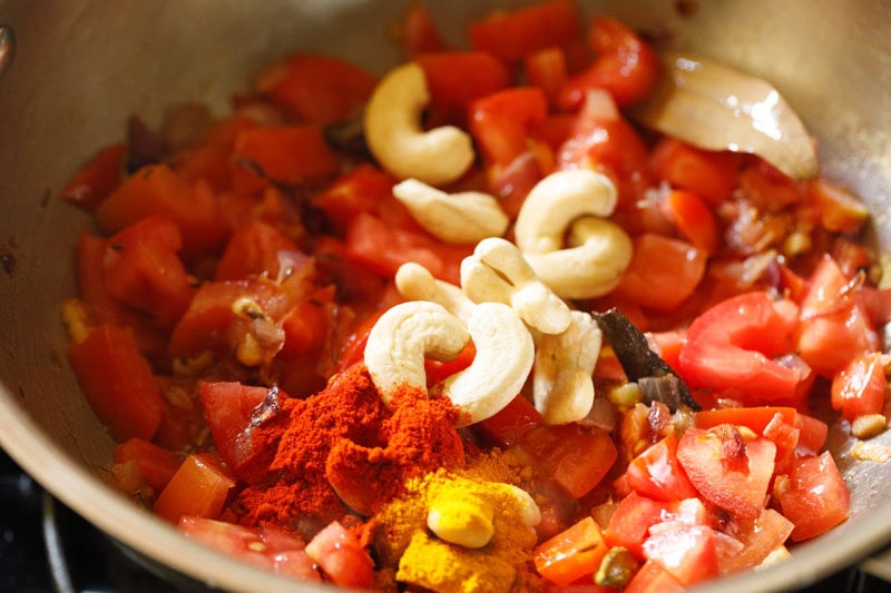 Cashews added to onions and tomatoes in pan.