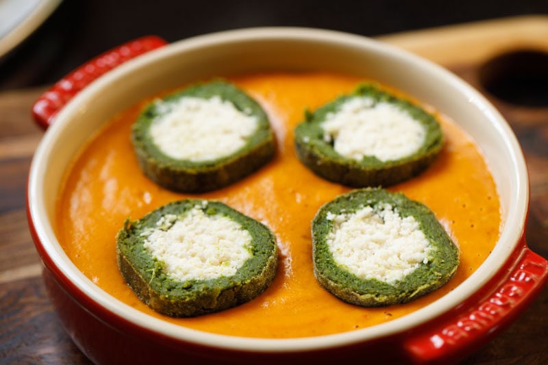 Halved palak kofta placed on orange gravy to make shaam savera