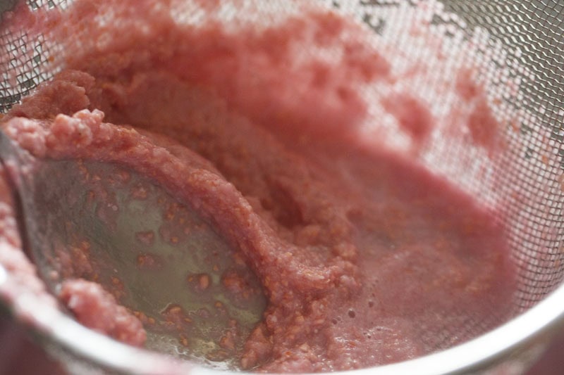 Thick pink pomegranate pulp in mesh strainer.