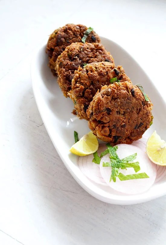 shami kabab served on a white platter with onion slices and lemon wedges.